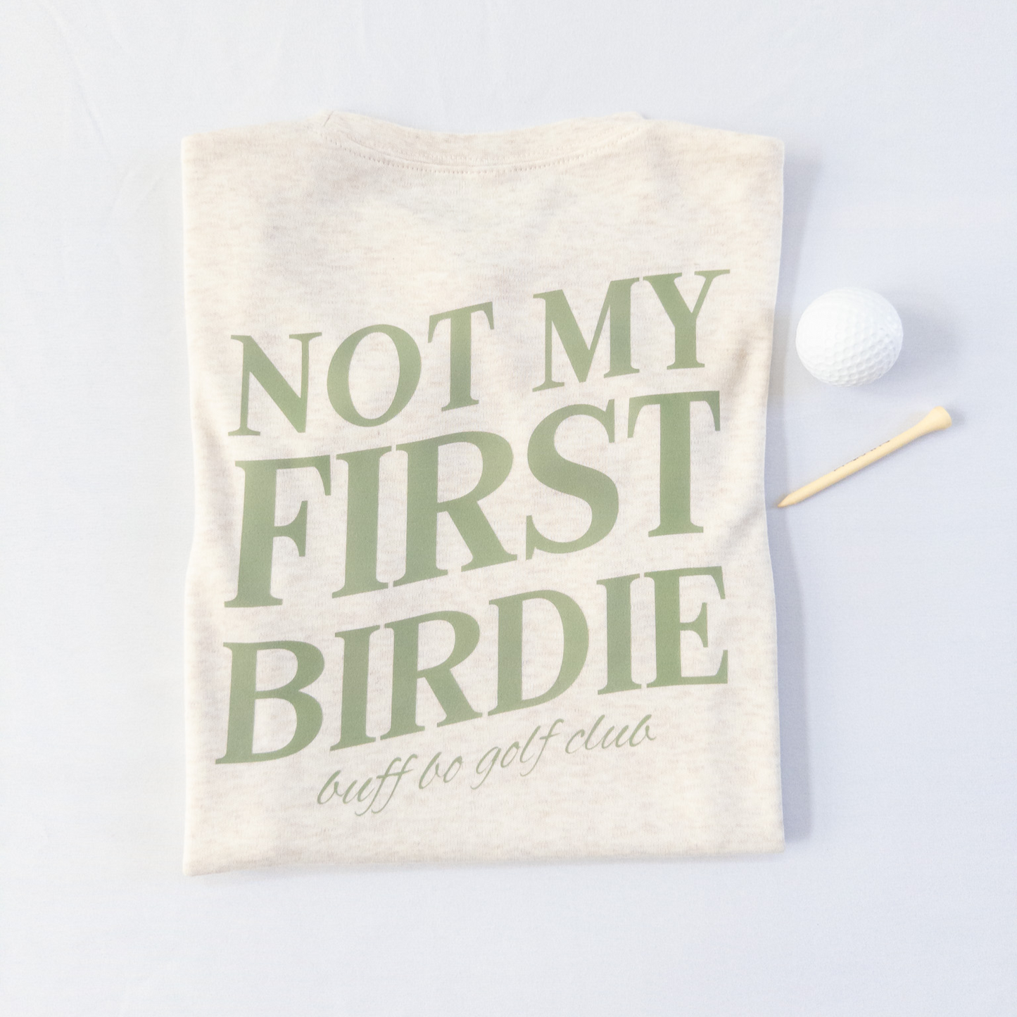 Beige towel with green text 'Not My First Birdie' on a light gray background