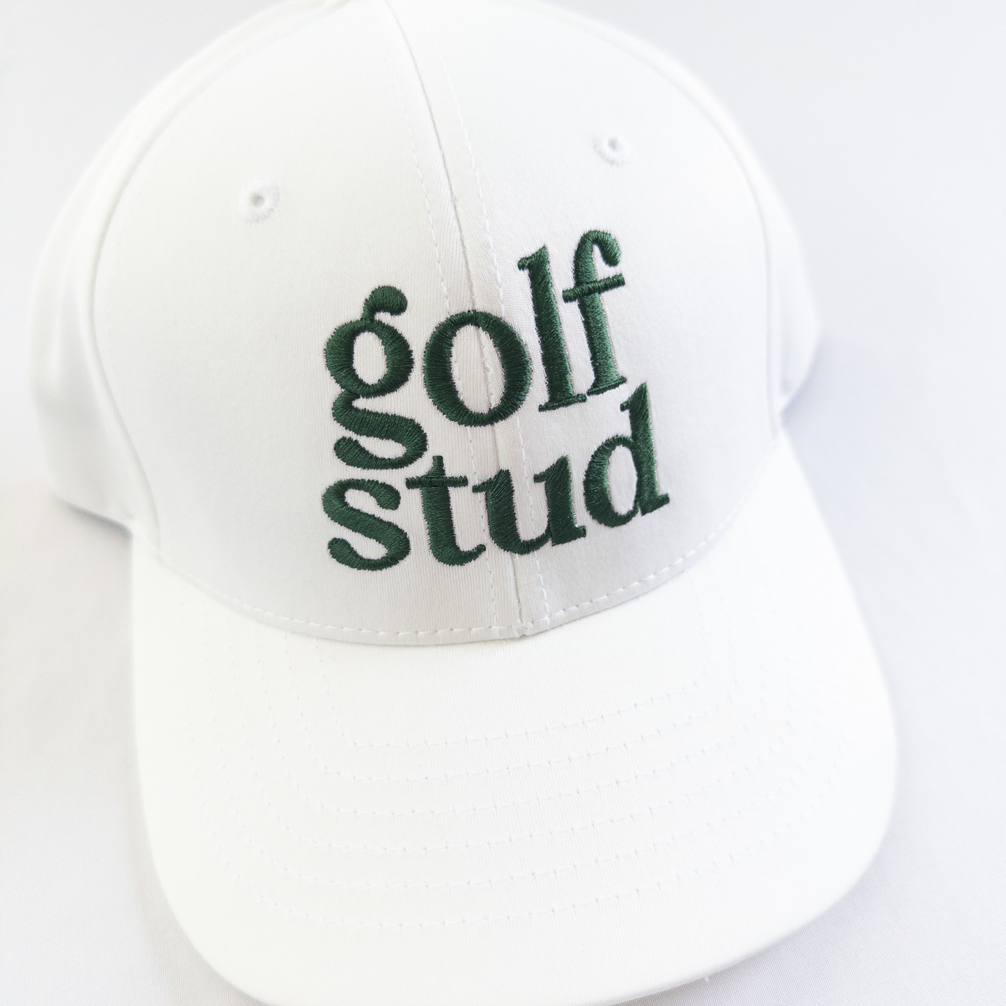 White golf hat with bold green embroidered text reading 'golf stud,' minimalist and stylish golf accessory perfect for young golfers and golf enthusiasts, displayed on a clean white background.