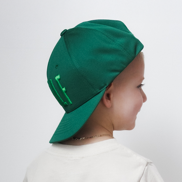 Child wearing a white t-shirt with a graphic design and a green cap on a plain background