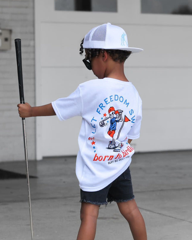 Child holding a golf club and wearing a 'Freedom' t-shirt in front of a garage.