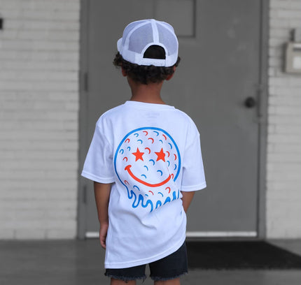 Child wearing a white t-shirt with a colorful design, standing in front of a building.
