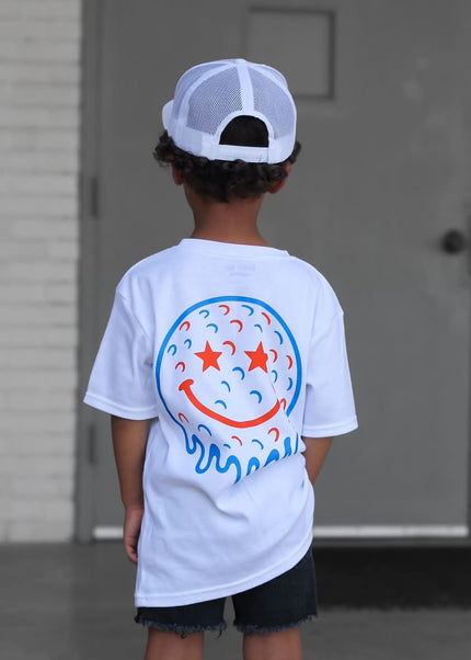 Child wearing a white t-shirt with a colorful design, standing in front of a building.