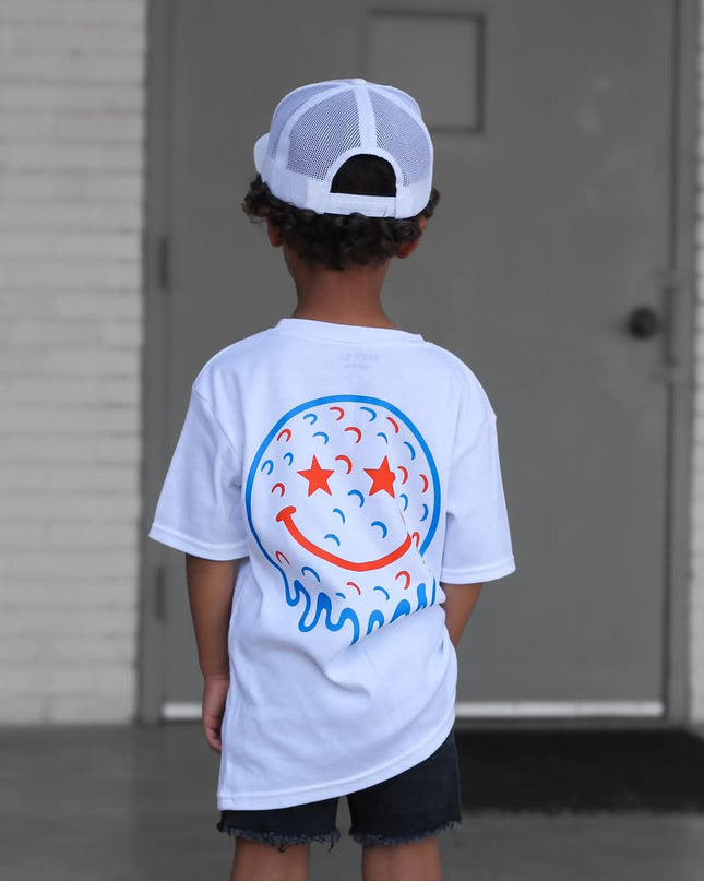 Child wearing a white t-shirt with a colorful design, standing in front of a building.