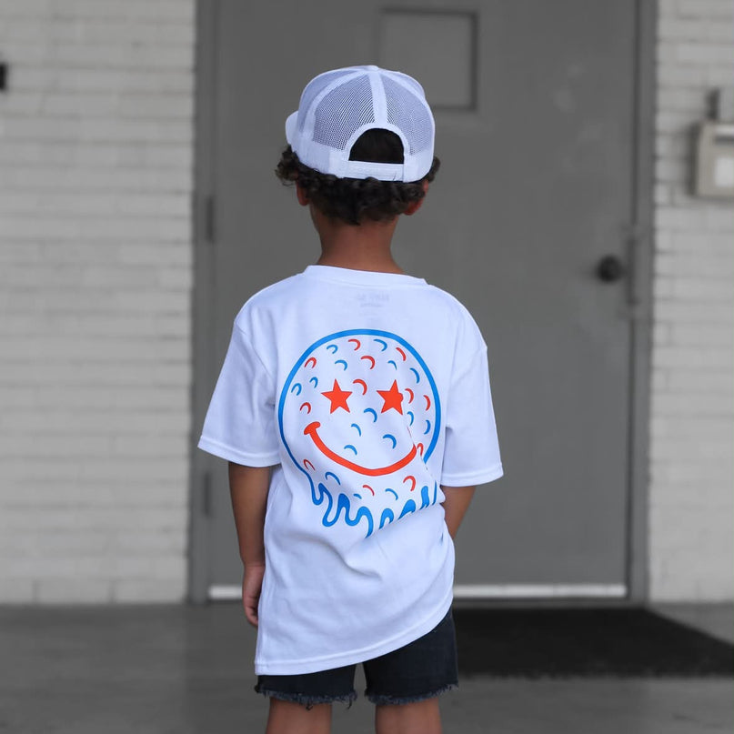 Child wearing a white t-shirt with a colorful design, standing in front of a building.