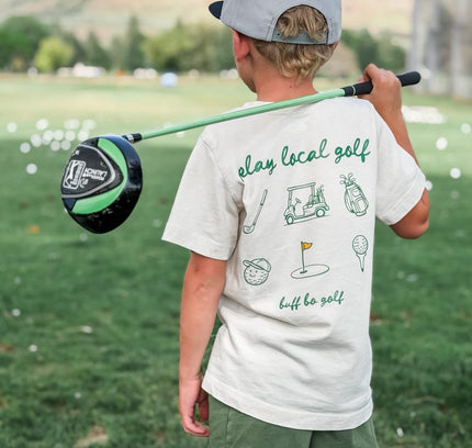 Child holding a golf club on a golf course with mountains in the background