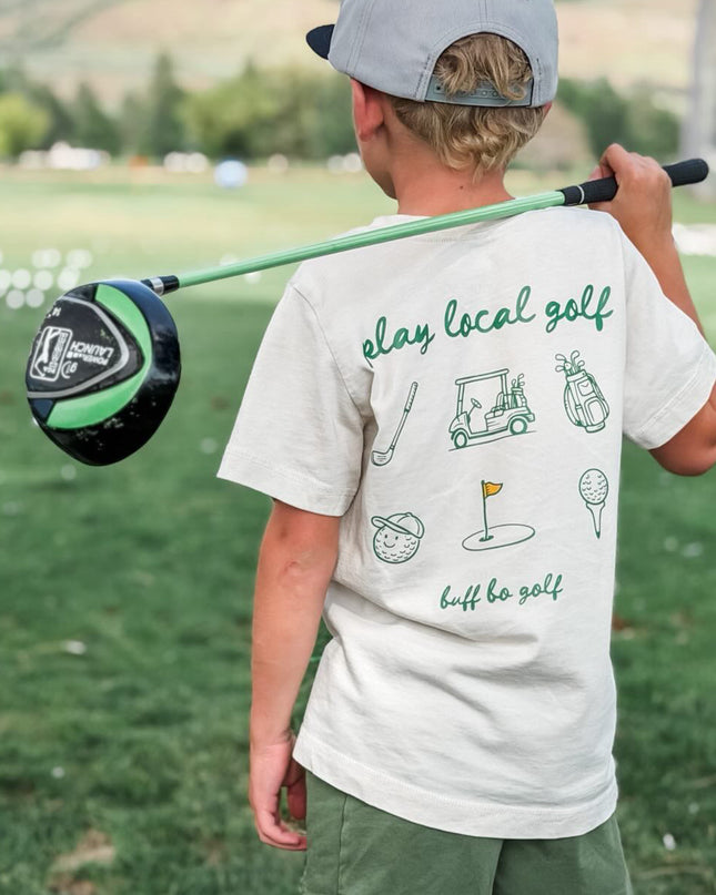 Child holding a golf club on a golf course with mountains in the background