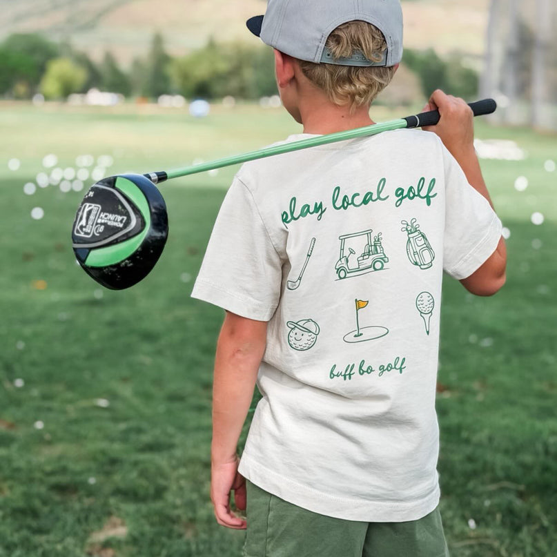 Child holding a golf club on a golf course with mountains in the background