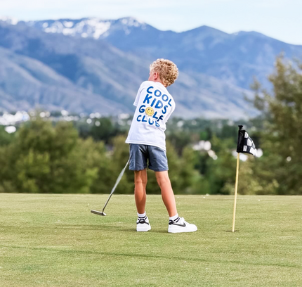 Child playing golf on a scenic course with mountains in the background