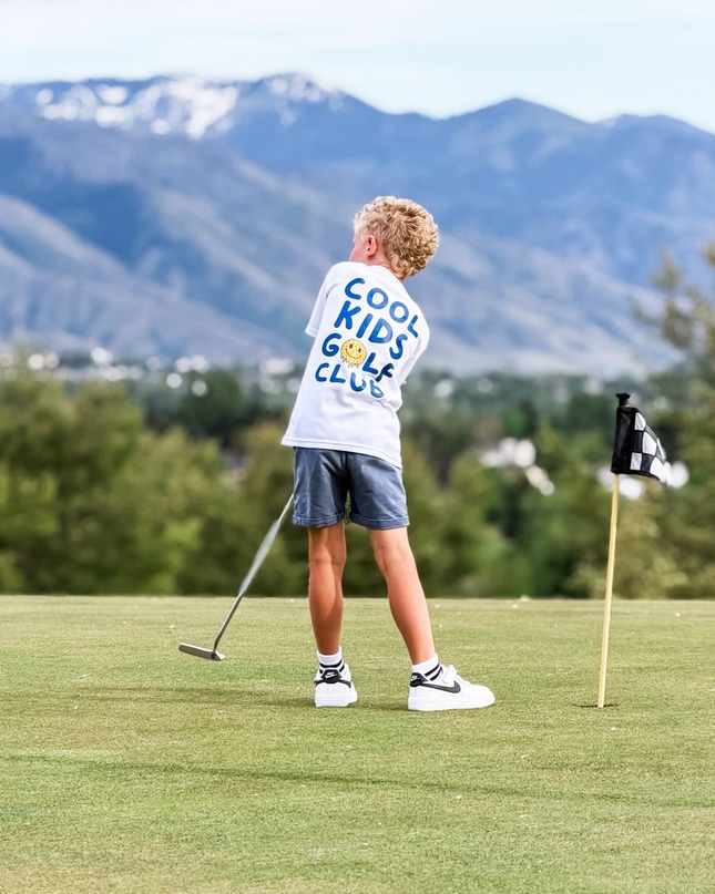 Child playing golf on a scenic course with mountains in the background