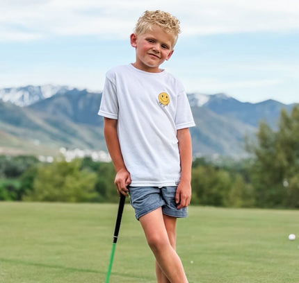 Young boy holding a golf club on a golf course with mountains in the background