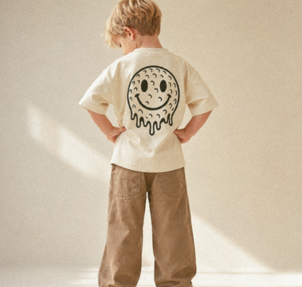 Child wearing a beige t-shirt with a smiley face design on the back, standing against a plain background.