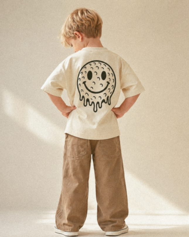 Child wearing a beige t-shirt with a smiley face design on the back, standing against a plain background.