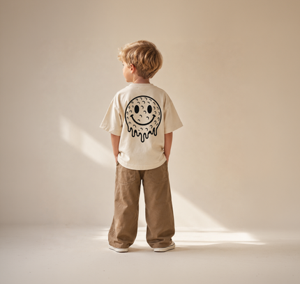 Child wearing a biege t-shirt with a smiley face design on a plain background