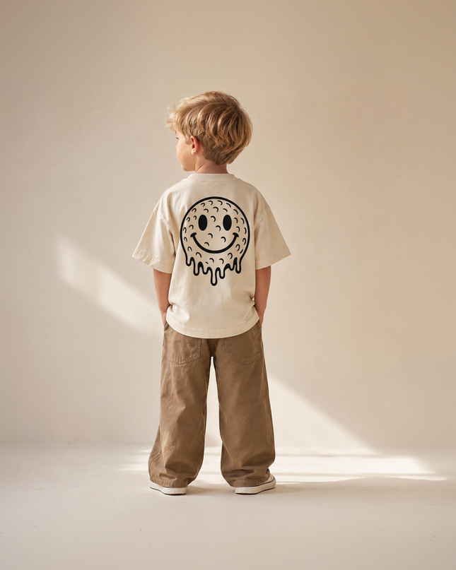 Child wearing a biege t-shirt with a smiley face design on a plain background