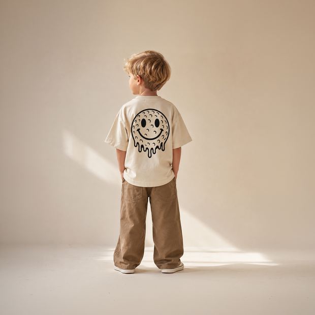 Child wearing a biege t-shirt with a smiley face design on a plain background