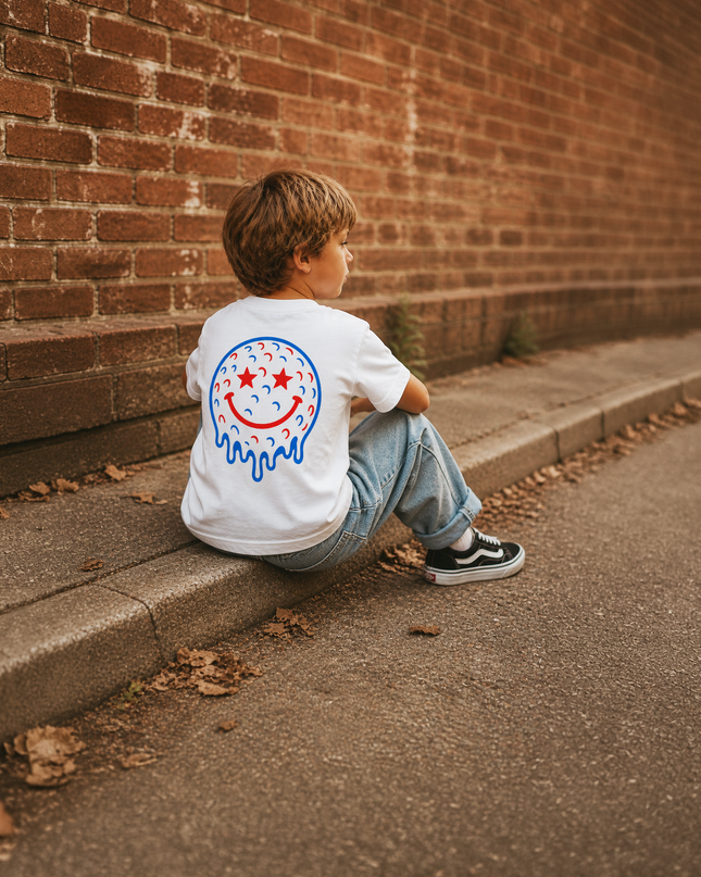 Child sitting on a step wearing a white t-shirt with a colorful logo against a brick wall.