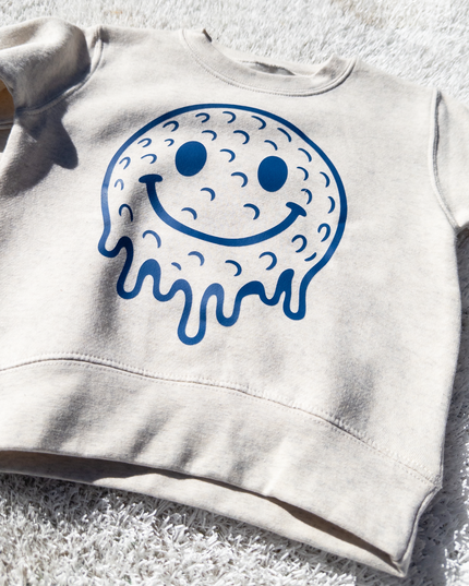 Beige sweatshirt with a blue smiley face design on a textured surface