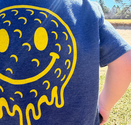 Person wearing a blue t-shirt with a yellow smiley face design outdoors.