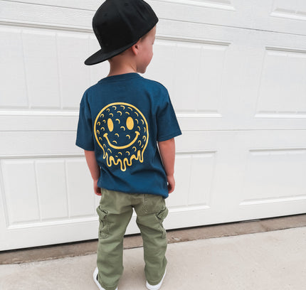 Child wearing a blue t-shirt with a smiley face design, standing in front of a white garage door.