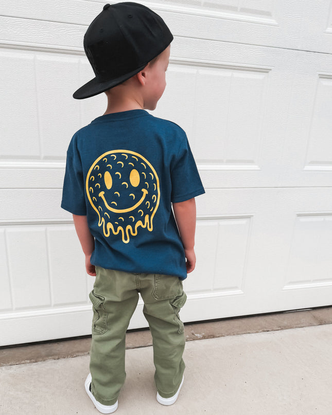 Child wearing a blue t-shirt with a smiley face design, standing in front of a white garage door.