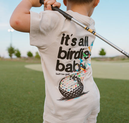 Child wearing a t-shirt with a golf-themed design on a golf course
