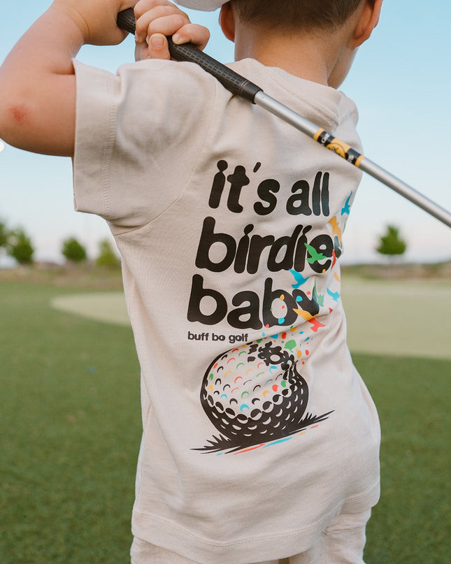 Child wearing a t-shirt with a golf-themed design on a golf course