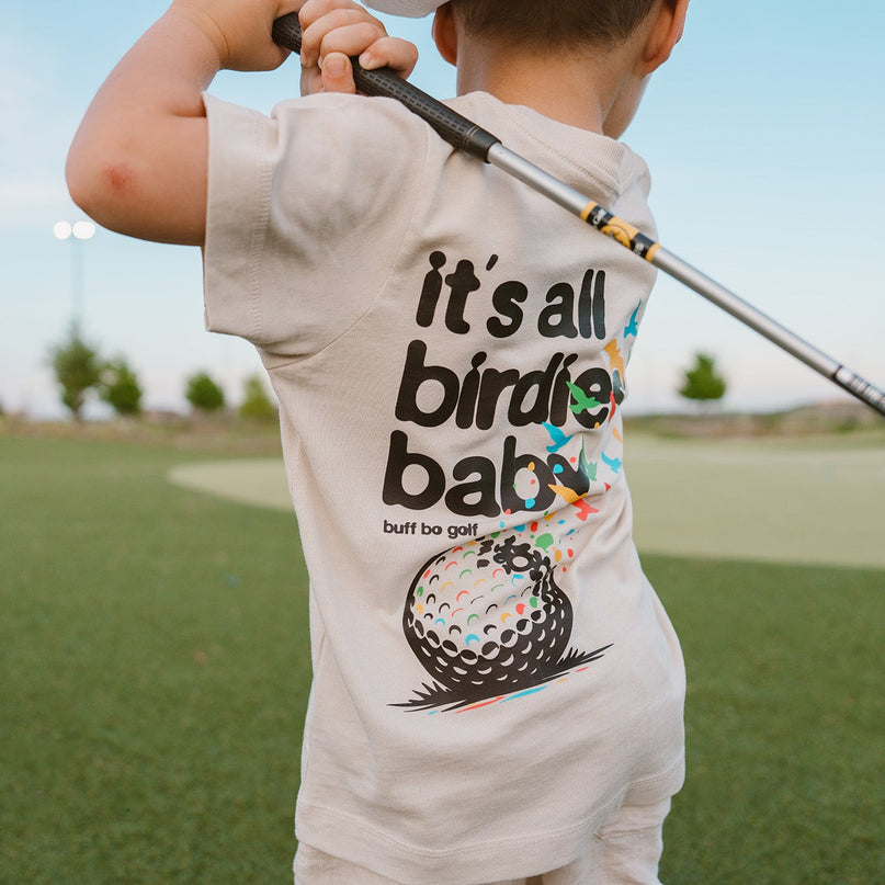 Child wearing a t-shirt with a golf-themed design on a golf course