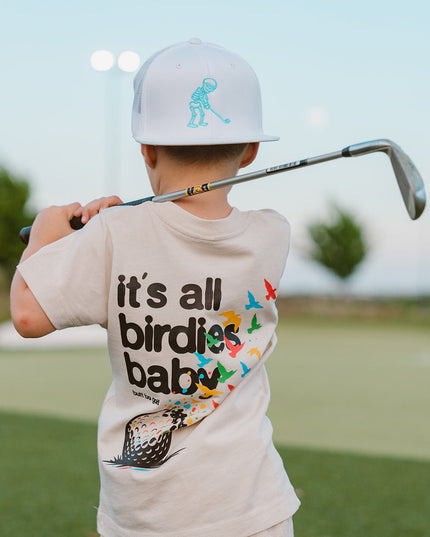 Child holding a golf club on a golf course wearing a t-shirt with text and graphics.