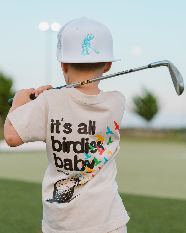 Child holding a golf club on a golf course wearing a t-shirt with text and graphics.