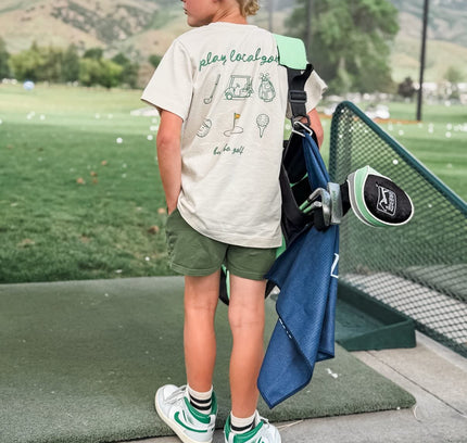 Child holding a golf club on a golf course with mountains in the background