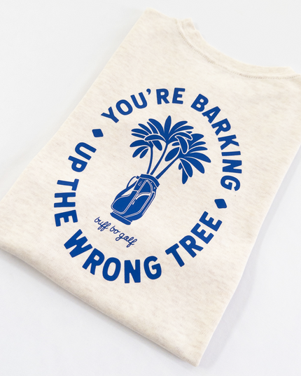 Beige kids golf t-shirt featuring bold blue graphic with palm trees in a golf bag and playful text reading 'You're Barking Up The Wrong Tree,' from Buff Bo Golf apparel collection, displayed on a light background.