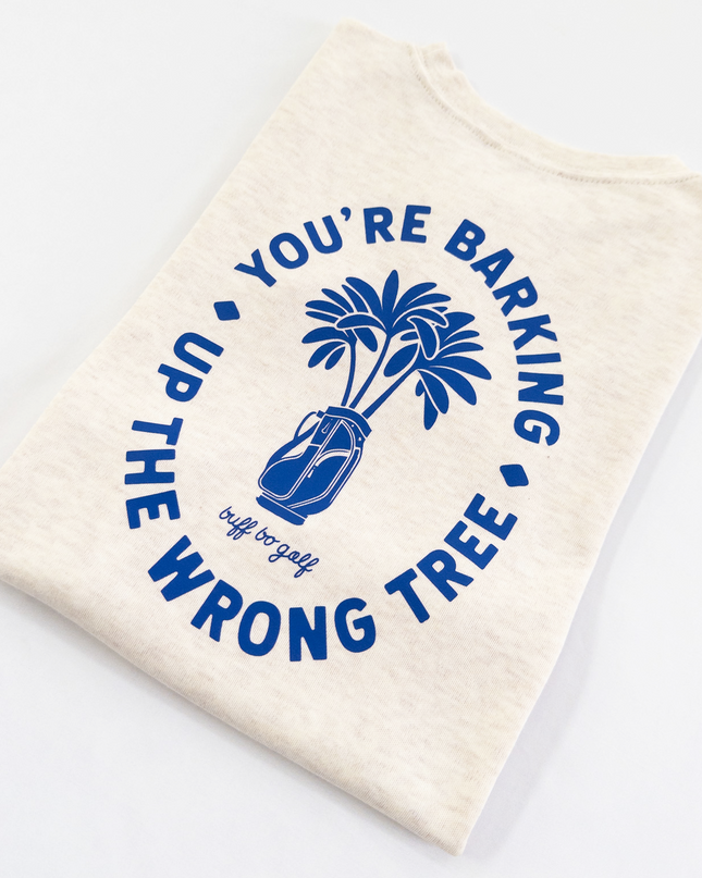 Beige kids golf t-shirt featuring bold blue graphic with palm trees in a golf bag and playful text reading 'You're Barking Up The Wrong Tree,' from Buff Bo Golf apparel collection, displayed on a light background.