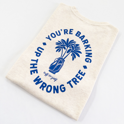 Beige kids golf t-shirt featuring bold blue graphic with palm trees in a golf bag and playful text reading 'You're Barking Up The Wrong Tree,' from Buff Bo Golf apparel collection, displayed on a light background.