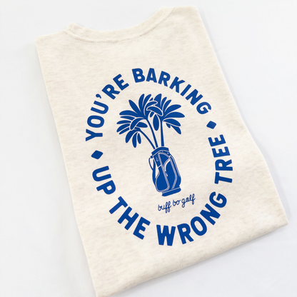 Beige kids golf t-shirt featuring bold blue graphic with palm trees in a golf bag and playful text reading 'You're Barking Up The Wrong Tree,' from Buff Bo Golf apparel collection, displayed on a light background.
