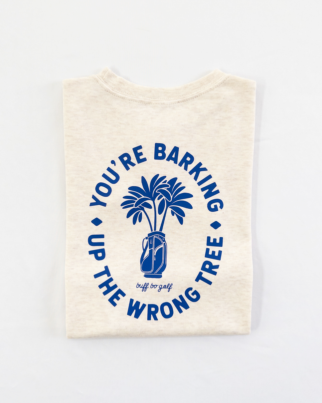 Beige kids golf t-shirt featuring bold blue graphic with palm trees in a golf bag and playful text reading 'You're Barking Up The Wrong Tree,' from Buff Bo Golf apparel collection, displayed on a light background.