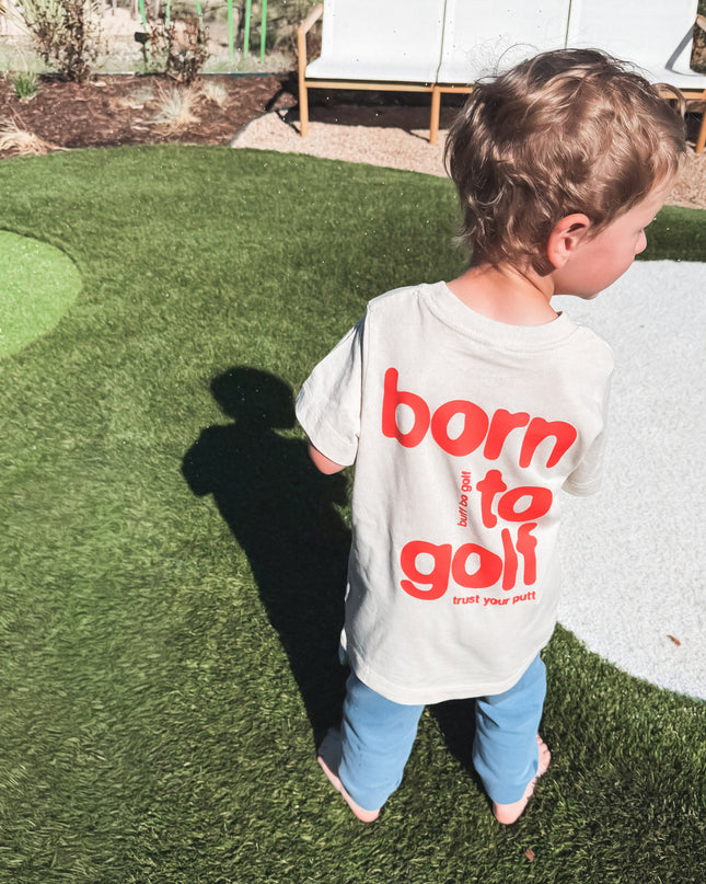 Child wearing a 'born to golf' shirt on a putting green