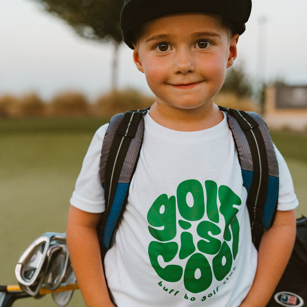 Child wearing a 'Golf is Cool' t-shirt with a golf club and bag in the background