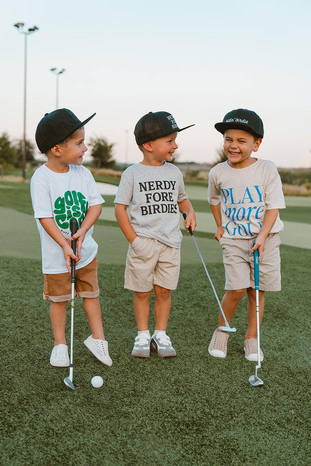 Three children in matching outfits with golf equipment on a golf course.