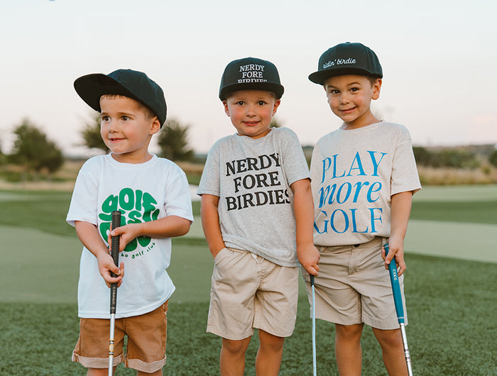 Three children on a golf course wearing themed t-shirts and hats.