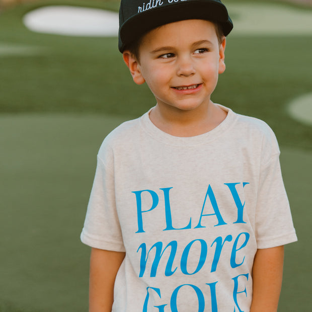 Child wearing a t-shirt with 'Play more golf' on a golf course