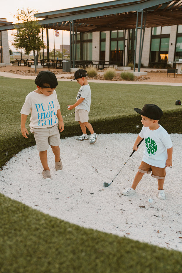 Three children playing golf on a mini course with a building in the background.