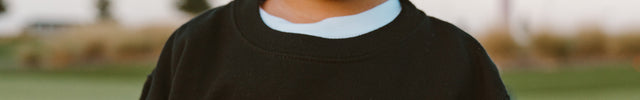 Child wearing a black sweatshirt with 'buff bo outfitters' text outdoors.