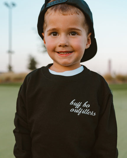 Child wearing a black sweatshirt with 'buff bo outfitters' text outdoors.