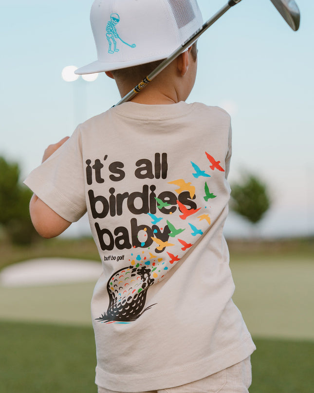 Child holding a golf club on a golf course wearing a shirt with a humorous golf-themed design.