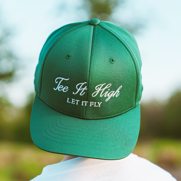Green cap with 'Tee It High Let It Fly' text against a blurred outdoor background
