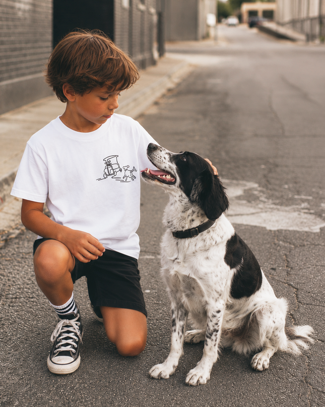 A young boy kneeling on a city street next to a black and white dog, wearing a white t-shirt with a black graphic of a coffee cup and espresso machine.