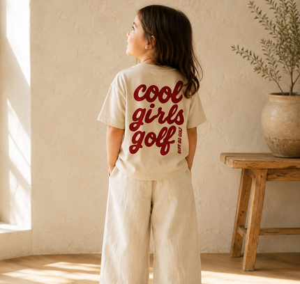 Child wearing a 'cool girls golf' t-shirt in a room with natural light