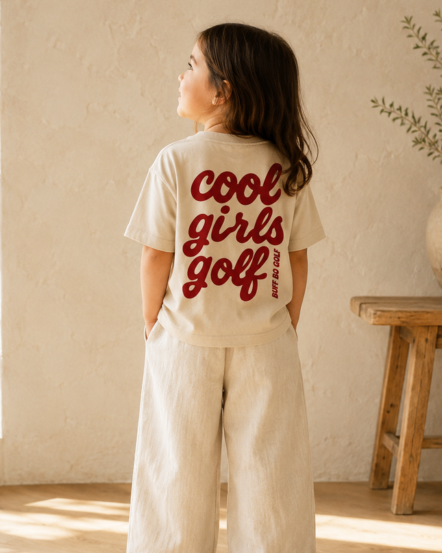 Child wearing a 'cool girls golf' t-shirt in a room with natural light
