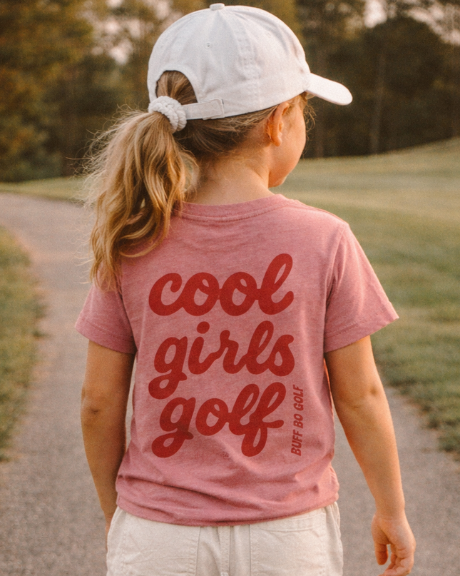 Child wearing a 'cool girls golf' t-shirt walking on a path outdoors.