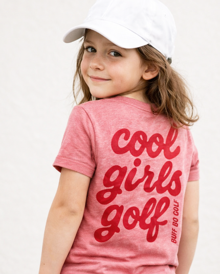 Young girl wearing a pink 'cool girls golf' t-shirt and white cap on a plain background